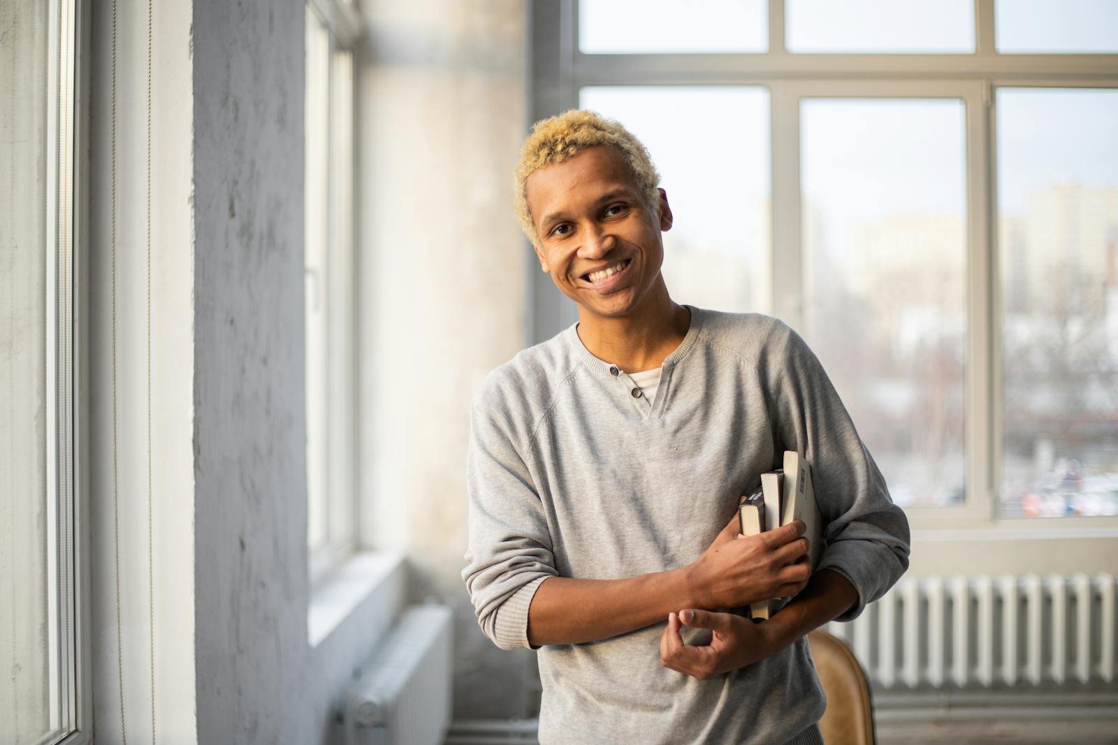 Charismatic African American man with books, smiling in a sunlit apartment.